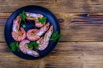 Plate with prepared shrimps and parsley leaves on a wooden table. Top view