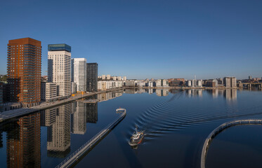 Obraz premium Train bridge view at the bay Årstaviken, apartment skyscrapers reflecting and a tug boat passing bridge, a tranquil early sunny spring day in Stockholm