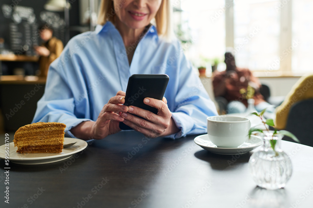 Aufkleber close-up of mature female consumer using smartphone by table served with cup of tea and piece of cak