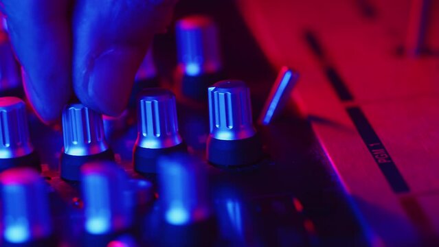 DJ toggling the switch and accurately turning the knobs on the mixer close up during the session of the sound studio recording in a color light