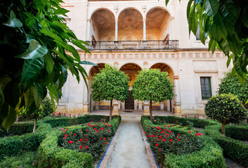 Fototapeta na wymiar 16th-century tiled gardens in the Casa de Pilatos palace with green plants and red flowers. Renaissance architecture style arches. Sevilla, Andalusia, Spain.