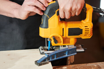 caucasian worker's hands adjust the jigsaw before starting work