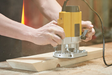 chips scatter in different directions when processing the edge of a wooden workpiece with a manual milling cutter, which is held by the hands of a Caucasian worker