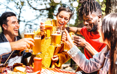Young friends toasting beer pint at brewery garden venue - Genuine food beverage life style concept with guys and girls sharing happy hour together at open air restaurant dehor - Vivid contrast filter