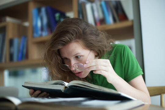 tired overworked, exhausted young woman in glasses college or university student is study hard in library, lesson, problem with eyes, myopic purblind. Vision eyes problems, myopia, blindness. 