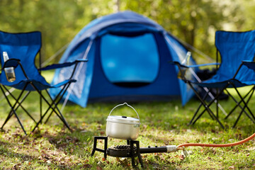 food cooking, tourism and travel concept - close up of camping pot on tourist gas burner at tent...