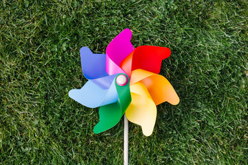ecology, environment and sustainable energy concept - close up of multicolored pinwheel on green lawn or grass