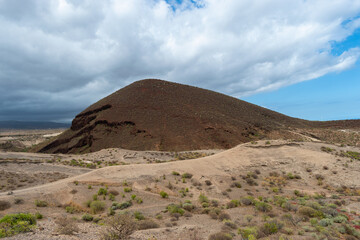 Montaña volcánica, rodeada tierra color beige, paisaje protegido, con cielo azul