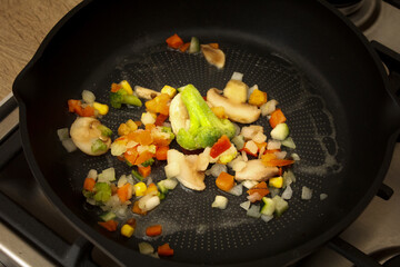 Frozen vegetables are fried in a pan. onions, mushrooms, cauliflower and carrots in a pan