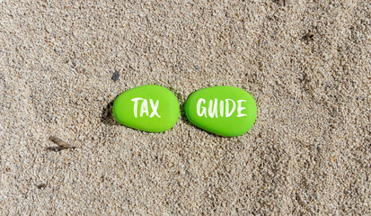 Tax guide symbol. Concept words Tax guide on beautiful green stone. Beautiful sand sea beach background. Business and Tax guide concept. Copy space.