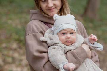 A young mother holds a charming little son in her arms. The kid looks at the camera and smiles. Portrait of a beautiful chubby 4-month-old baby.