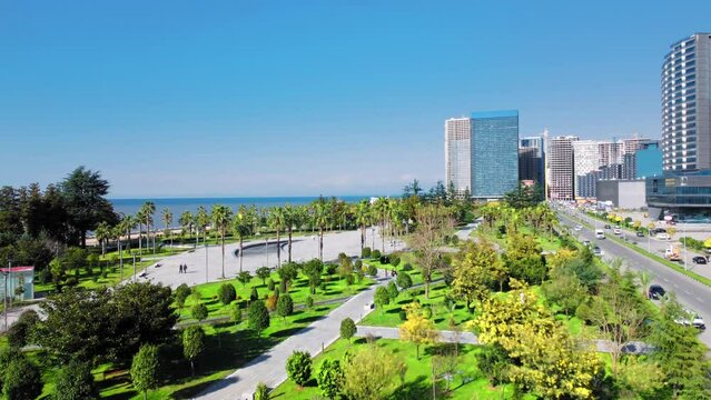 Resort town of Batumi in Georgia. Aerial view of green park on sunny day against background of sea. Lehi and Maria Kaczynski Park in city. Beautiful green landscaping. Infrastructure, mountains
