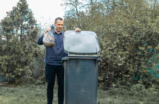 Man throwing out black eco-friendly recyclable trash bag in to big plastic green garbage container. Take out the trash