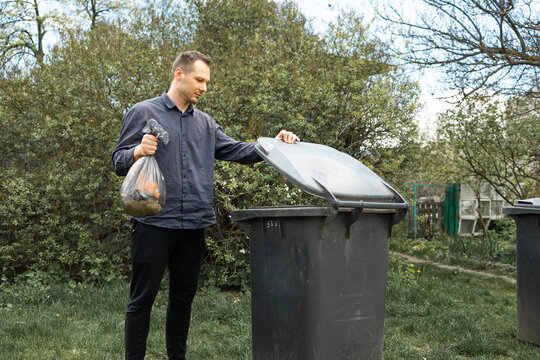 Man throwing out black eco-friendly recyclable trash bag in to big plastic green garbage container. Take out the trash