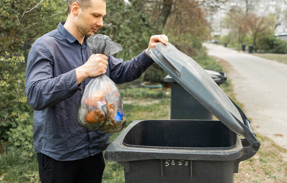 Man throwing out black eco-friendly recyclable trash bag in to big plastic green garbage container. Take out the trash