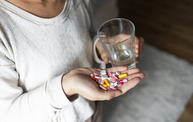 Asian woman in one hand handful of tablets, in other glass of clean water close up. Lot of pills. large dose.