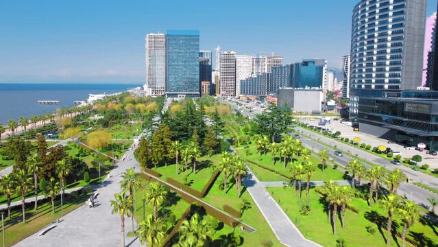 Resort town of Batumi in Georgia. Aerial view of green park on sunny day against background of sea. Lehi and Maria Kaczynski Park in city. Beautiful green landscaping. Infrastructure, mountains