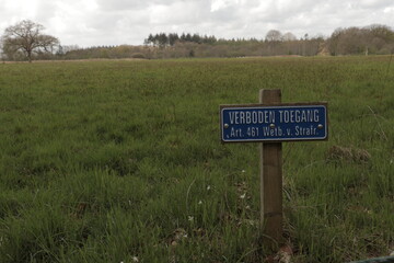 No entry sign in front of green field and forest. The Dutch words 'Verboden Toegang' mean No entry in English.