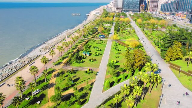 Resort town of Batumi in Georgia. Aerial view of green park on sunny day against background of sea. Lehi and Maria Kaczynski Park in city. Beautiful green landscaping. Infrastructure, mountains