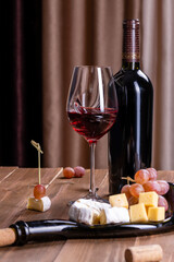 A glass and a bottle of red wine, a plate of cheese and grapes