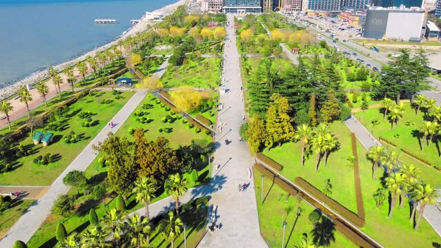 Resort town of Batumi in Georgia. Aerial view of green park on sunny day against background of sea. Lehi and Maria Kaczynski Park in city. Beautiful green landscaping. Infrastructure, mountains