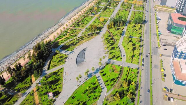 Resort town of Batumi in Georgia. Aerial view of green park on sunny day against background of sea. Lehi and Maria Kaczynski Park in city. Beautiful green landscaping. Infrastructure, mountains