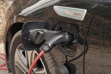 Black electric car charging using a black charger with red cable.