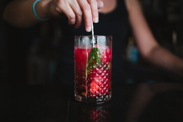 Bartender preparing a berries and lime mojito. She is stirring it using a bar spoon.