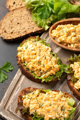 Egg salad sandwiches with greens and herbs on wooden board. Healthy food.