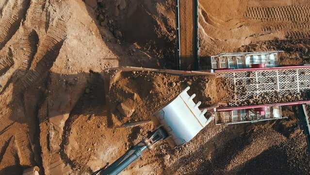 Crushing screening plant. Mining truck loading stones on sorting conveyor belt. Heavy machinery working for minerals extraction. Mining extractive industry.