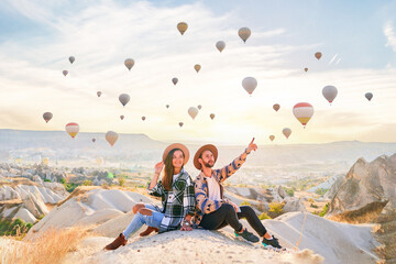 Traveling couple sitting together in scenic valley in Anatolia, Kapadokya. Flying hot air balloons...