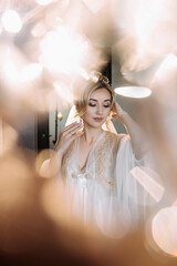 Blonde bride poses in a robe and tiara, wedding portrait. Reflections and reflections of glass. wedding photo in a light key