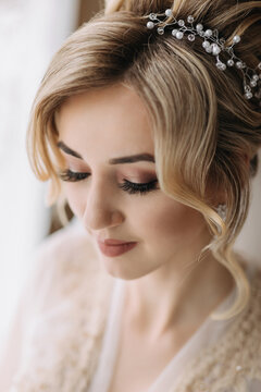 Blonde Bride with elegant hairstyle and tiara, in mantle, standing looking down. Nice makeup. Wedding photo