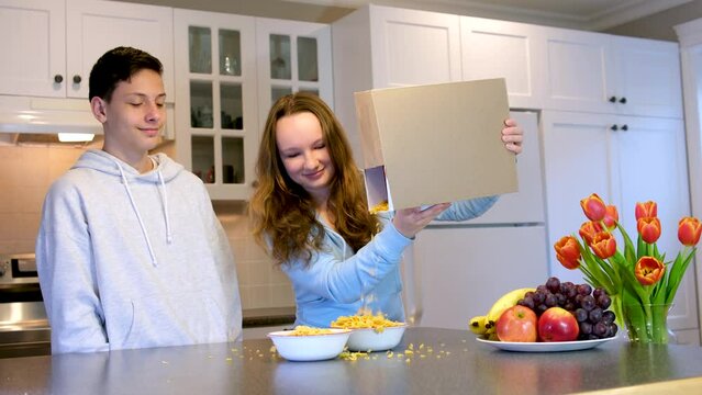 teenagers boys and girl cooking Breakfast poured from a box of cereal on the box can Your advertising empty space for text space delicious food spend time together fun brother and sister