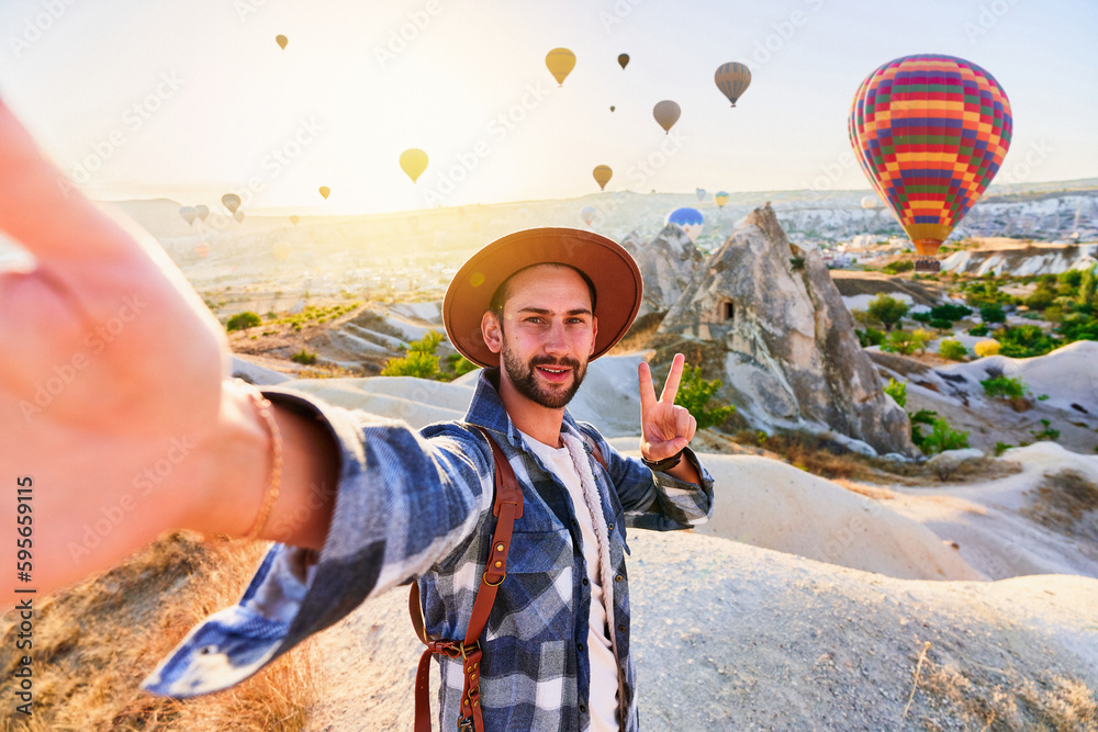 Wall mural happy bearded guy traveling blogger with victory sign takes selfie photo in nevsehir, goreme. beauti - Wall murals