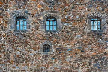 Antique stone wall with beautiful small windows. Bare tree branches lean over the windows.