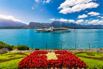 Flowerbed of the Swiss flag with boat cruise on the Thun lake and Alps mountains, Oberhofen,...