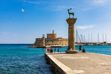 Mandraki port with deers statue, where The Colossus was standing and fort of St. Nicholas. Rhodes, Greece. Hirschkuh statue in the place of the Colossus of Rhodes, Rhodes, Greece - obrazy, fototapety, plakaty