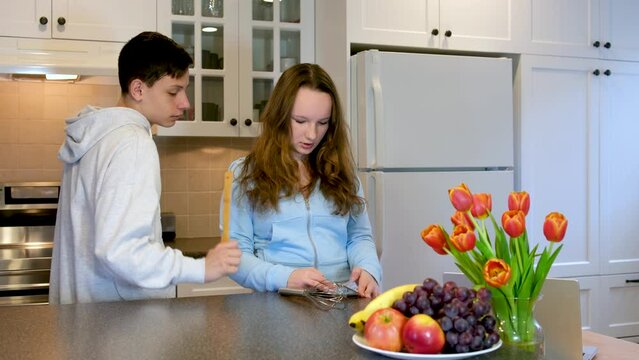 Romantic young couple cooking together in the kitchen, having great time together. Man and woman laughing teenagers read the news on the phone