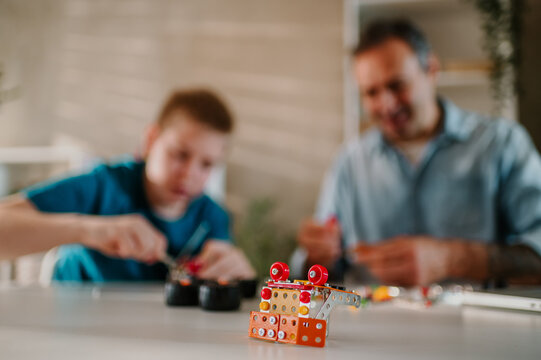 Focus on a metal toy part up front with a blurred background of a son and dad.