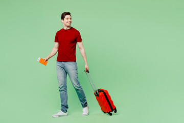 Traveler man wear casual clothes hold suitcase passport ticket isolated on plain pastel green...