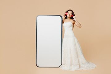 Full body young woman bride wears wedding dress posing big huge blank screen mobile cell phone with...