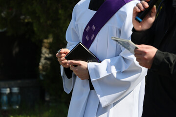 Ksiądz katolicki w komży z fioletowa stułą podczas celebracji pogrzebu. 