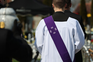 Ksiądz katolicki w komży z fioletowa stułą podczas celebracji pogrzebu.  - obrazy, fototapety, plakaty