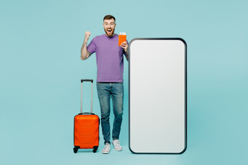 Traveler winner man wear casual clothes hold suitcase passport ticket big huge blank screen mobile cell phone isolated on plain green background. Tourist travel abroad in free spare time rest getaway.