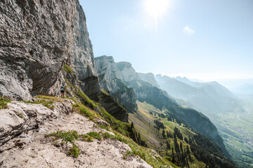 Sporty woman enjoys amazing view on the Churfürsten mountain range from hike trail below steep rock wall. Schnürliweg, Walensee, St. Gallen, Switzerland, Europe.