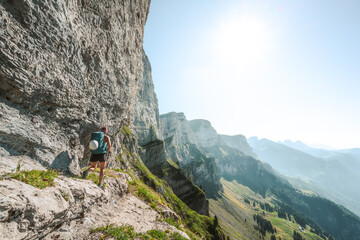 An athletic woman walks on hike trail below steep rock wall with amazing view on the Churfürsten...