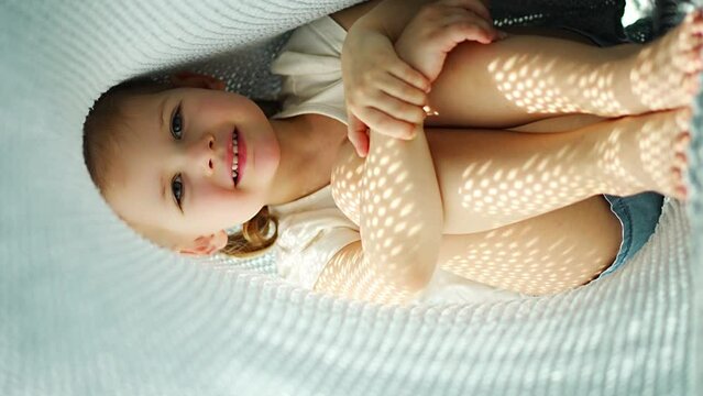 Little girl have a fun under blue knitted plaid in sunny morning