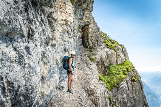 Sporty woman on rocky hike trail under steep rock wall enjoys view on lake Walensee. Schnürliweg, Walensee, St. Gallen, Switzerland, Europe.