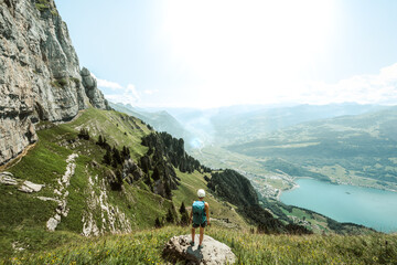Mountaineer stands on a rock next to the hiking trail and enjoys the view of lake Walensee and...